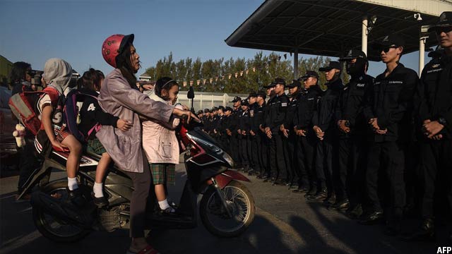 زن تایلندی که می خواهد کودکان اش را به مدرسه ببرد توسط گروهی از پولیس این کشور در نزدیکی معبد وات داماکایا متوقف شده است. تصویر از AFP / عکاس لیلیان سووانرومفا
