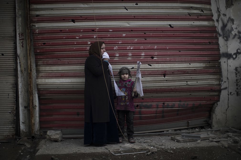 تصویری از دختر خردسال و مادرش که در اثر جنگ میان نیروهای عراقی و گروه داعش خانه شان را ترک کرده و در کنار یکی از جاده‌ها در شهر موصل عراق ایستاده‌اند. تصویر از AP.