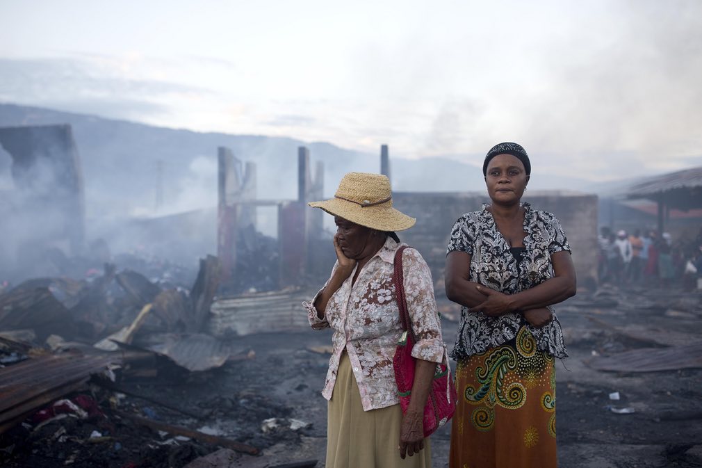 زنان ایستاده در میان بقایای ناشی از آتش سوزی در یکی از مراکز تجاری در شعر پورت آو پرینس. تصویر از AP.