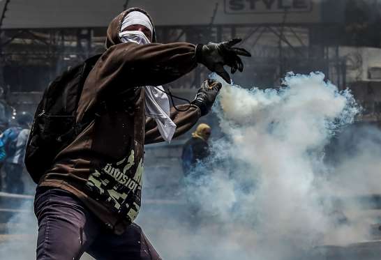 یک مظاهره کننده حین بازپرتاب نارنجک دودزا به سمت سربازان وینزویلایی. این تظاهرات بر علیه دولت نیکولاس مادورو رییس جمهور آن کشور از چندی به این سو راه‌اندازی شده است. / عکس: آژانس خبری فرانسه