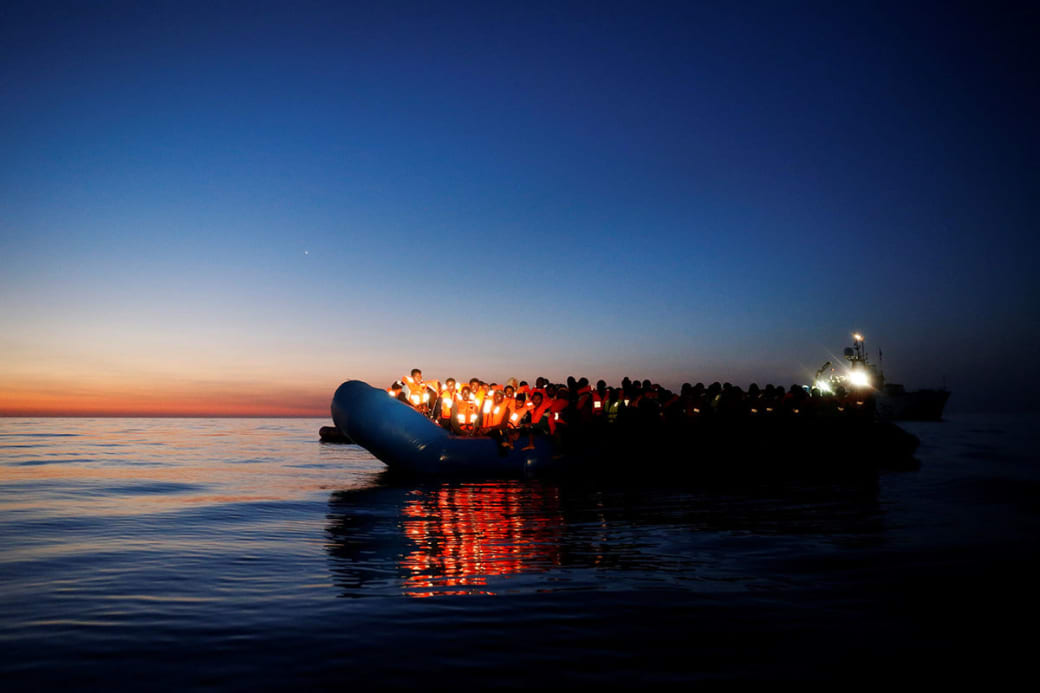 یک قایق پر از مهاجر چراغ به‌دست در انتظار ناجی. این تصویر توسط درین زمیت لوپی عکاس‌خبرنگار رویترز در سپیده‌دم از آنان شکار شده است.