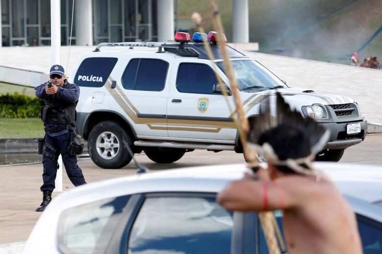 پولیس ضد شورش برازیل در جریان گرفتن اسلحه به سمت یک سرخ‌پوست برازیلی که به علت نقض حقوق مردم بومی آن کشور در برازیلیا پایتخت آن‌کشور دست به تظاهرات زده بودند. جالب این‌جاست که این برزیلی بومی با تیر و کمان خود اما پولیس را نشانه گرفته است. / عکس: رویترز
